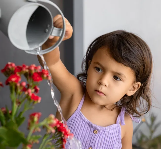 A girl watering red flowers with a watering can