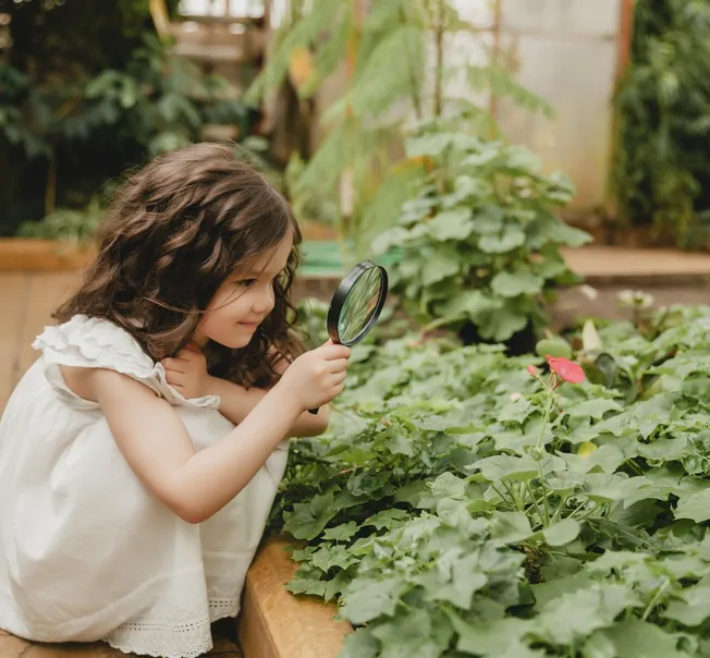 A girl exploring a garden bed with a magnifying glass