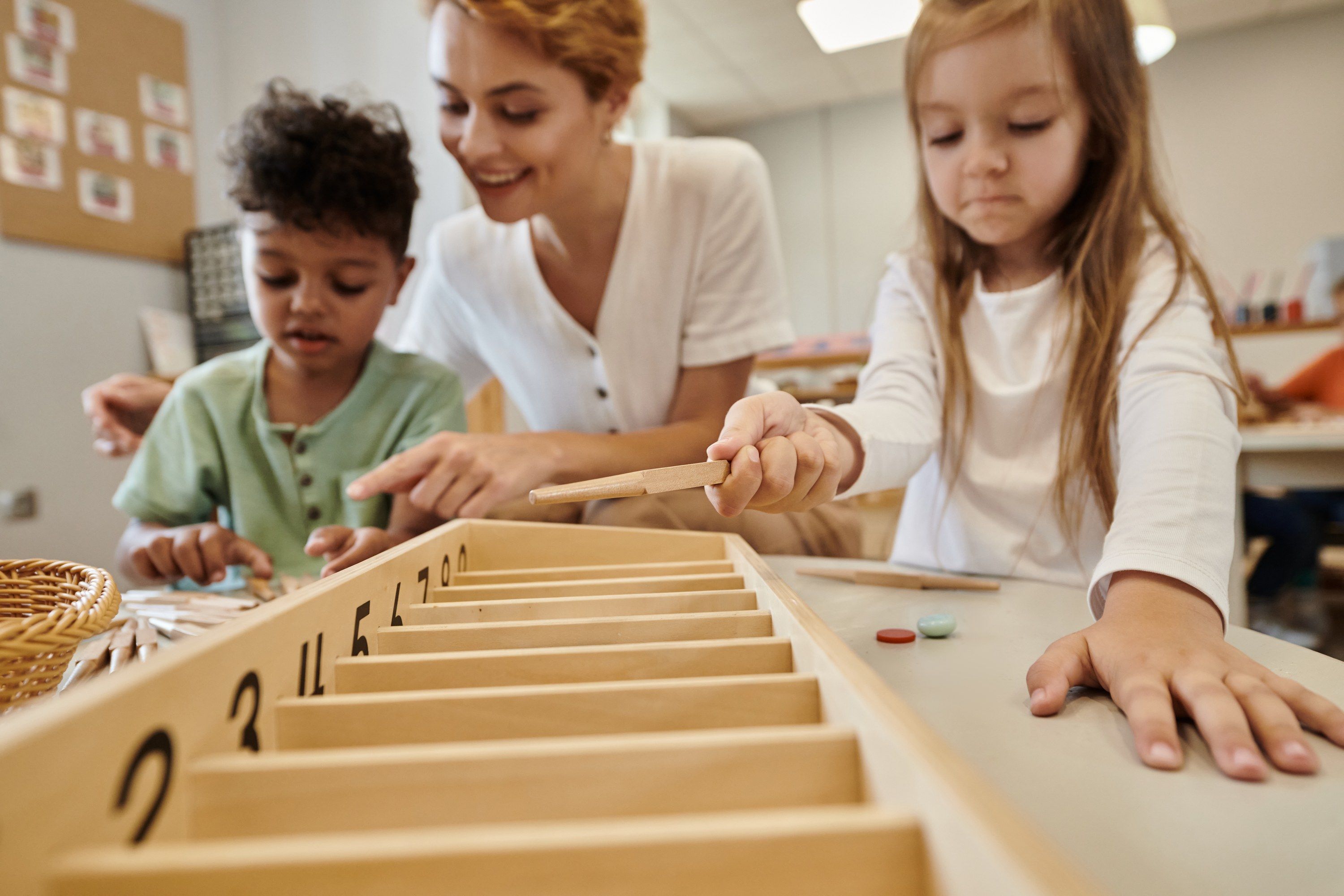 A teacher helping two children learn numbers with wooden materials