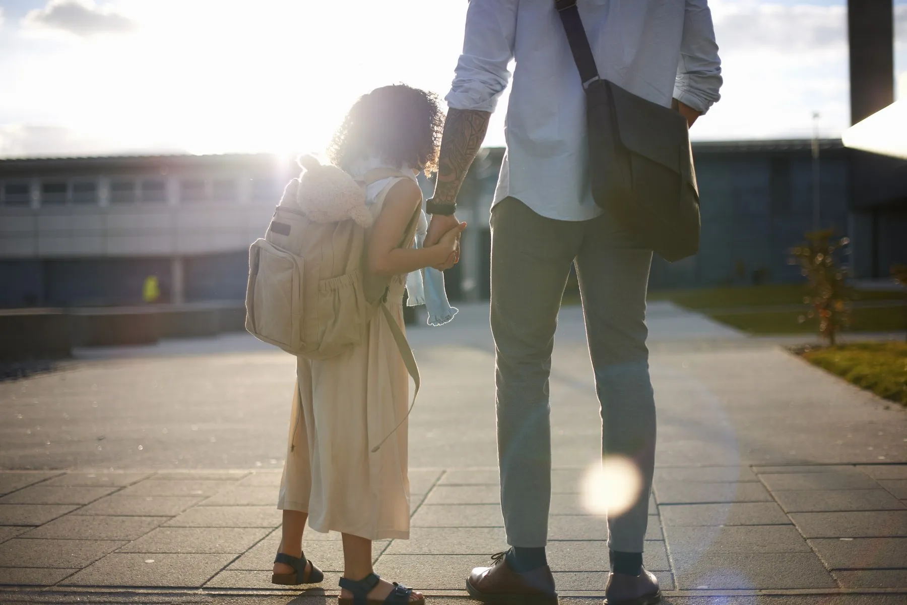 A child with a backpack holding a parent's hand on the way in