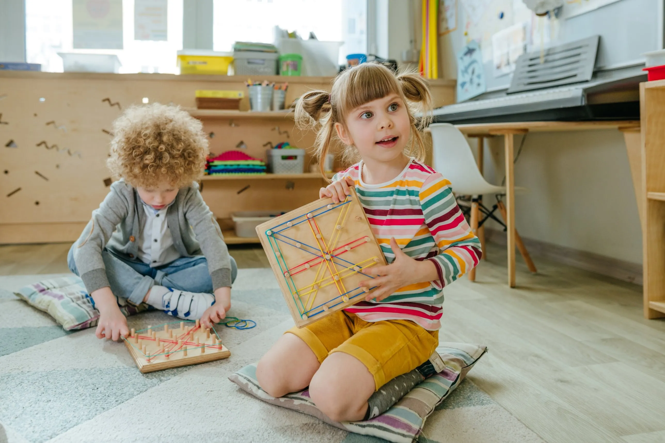 Two young children working with geoboards on a classroom rug